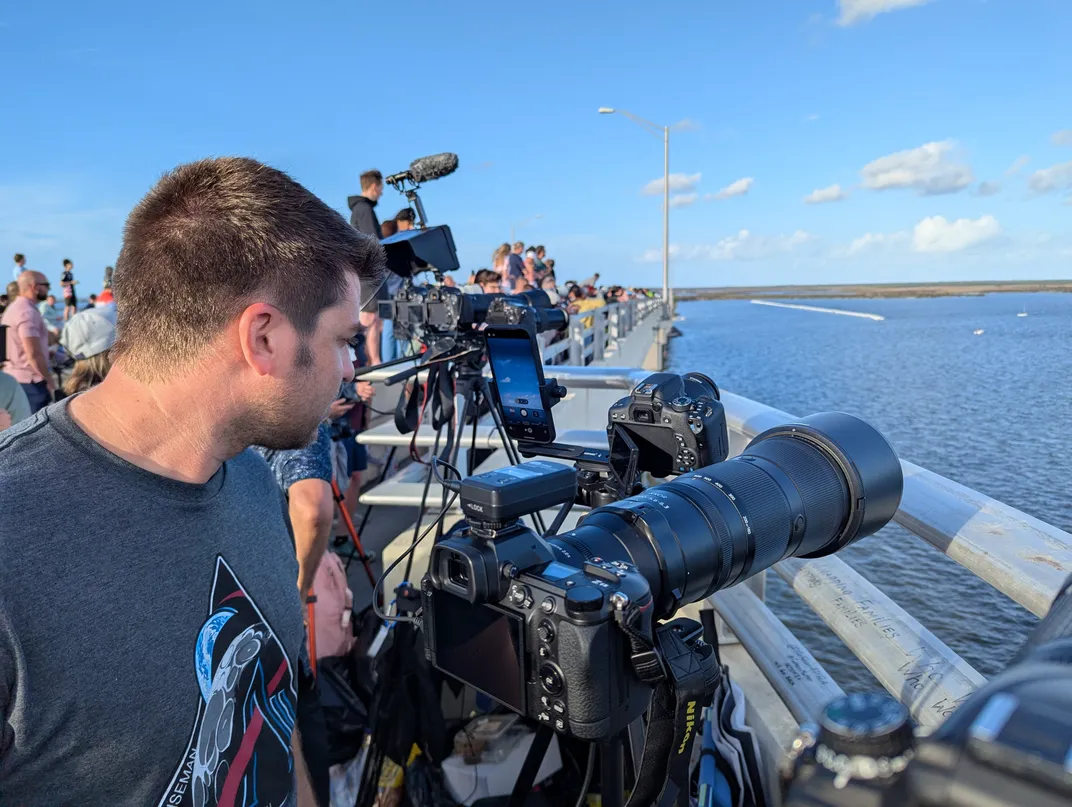 a man in front of a row of cameras on tripods on a bridge