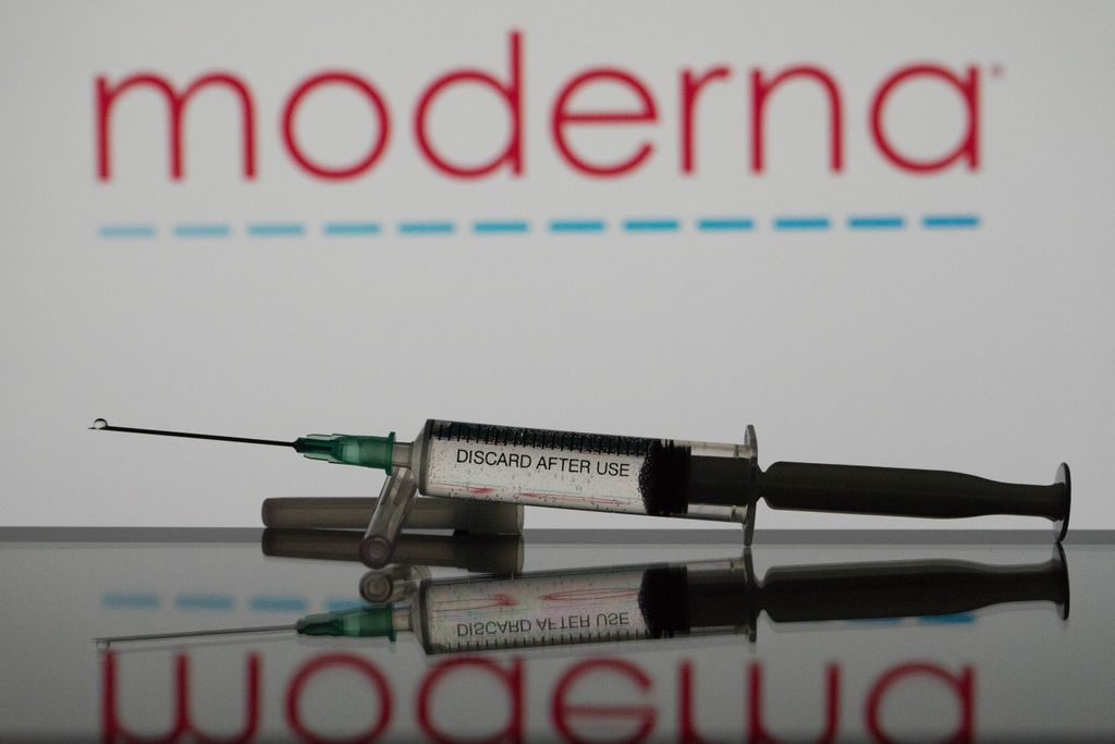A vaccine needle lies in front of a Moderna logo