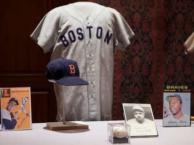 Hat and jersey worn by Ted Williams during his Red Sox reign. The autographed portraits, from left to right, are of Williams, Babe Ruth, and Hank Aaron. Foregrounded is a baseball signed by the members of the "Murderers' Row" 1927 Yankees.