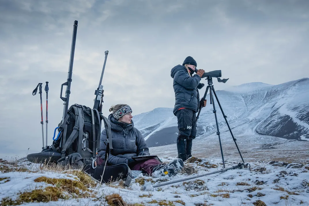 Upon locating one of their collared reindeer, Emma Djurberg—using the scope—calls out behavioral observations every ten seconds while Oline Eikeland, seated, takes notes.