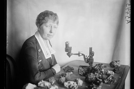 Black and white photo of Margaret W. Moodey sitting at a desk with a microscope and gemstones