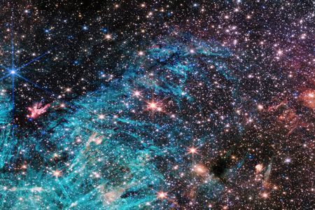 A multitude of stars packed together in a dense region of space, shining brightly in the surrounding darkness. A bright blue cloud in the lower half of the image with pitch black patches appearing within the cloud