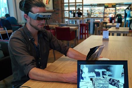 A SmartSpecs user looks at a magazine; the laptop screen shows his view.