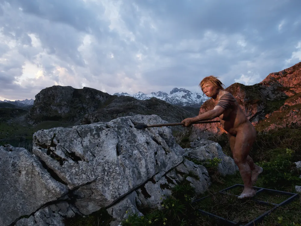 A model of a Neanderthal woman holding a spear next to a rock