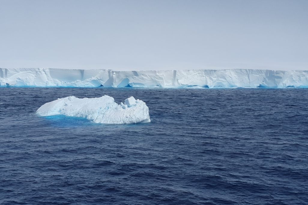 A small iceberg drifts in the ocean in front of a larger one