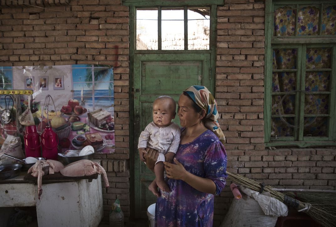 A Uyghur woman holds a child as they prepare food in her home during the Corban Festival on September 12, 2016.