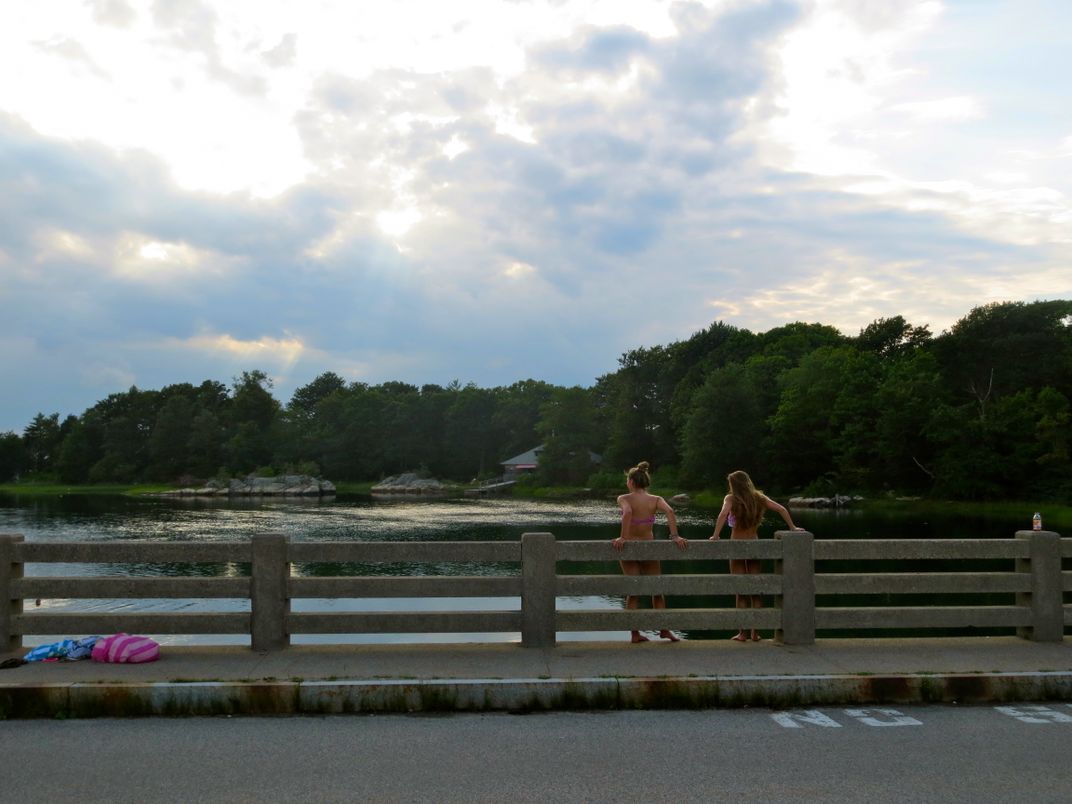 Two Girls Prepare To Jump Off A Bridge Into The River Below On A Summer 