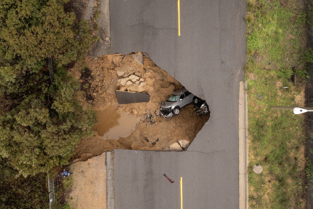 An aerial view of two cars lying in a sinkhole under a road.