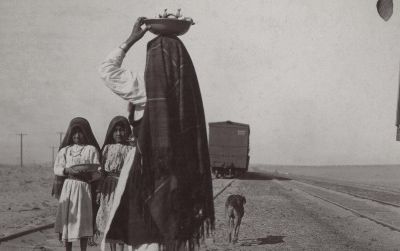 An Isleta woman and her children sell goods alongside a train track, circa late 1880s to early 1900s