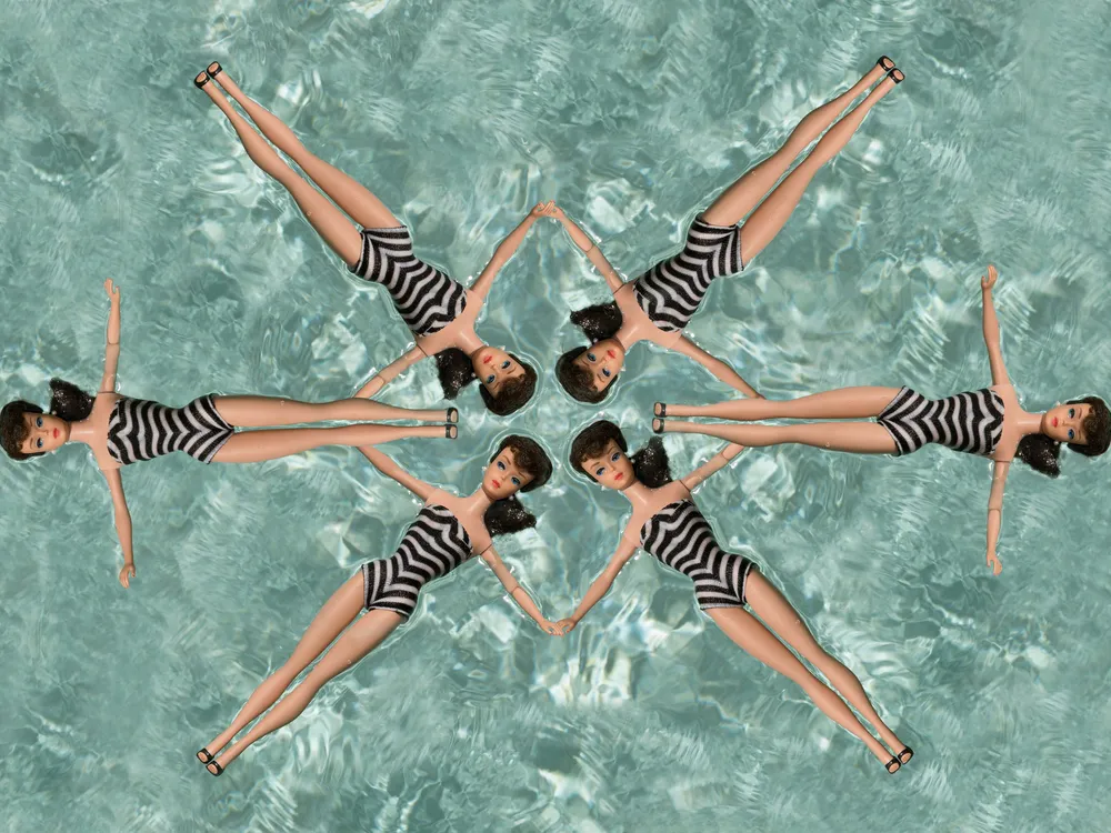 Six Barbie dolls in zebra-striped bathing suits form a synchronized formation in the pool