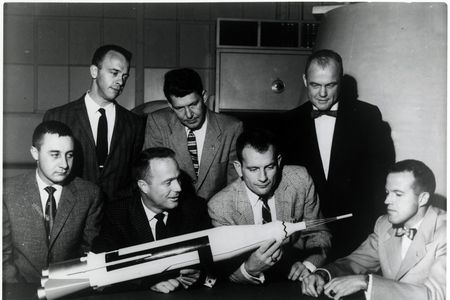 John Glenn, standing top right, looks at a model of the ship that took him to space with other astronauts from the Mercury space program in an undated photograph.