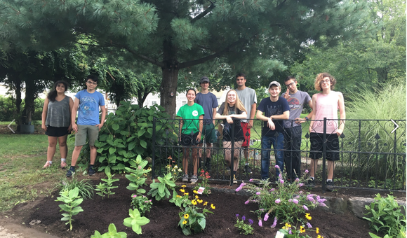 A group of young people stand in front of a pollinator garden in Lowell, MA