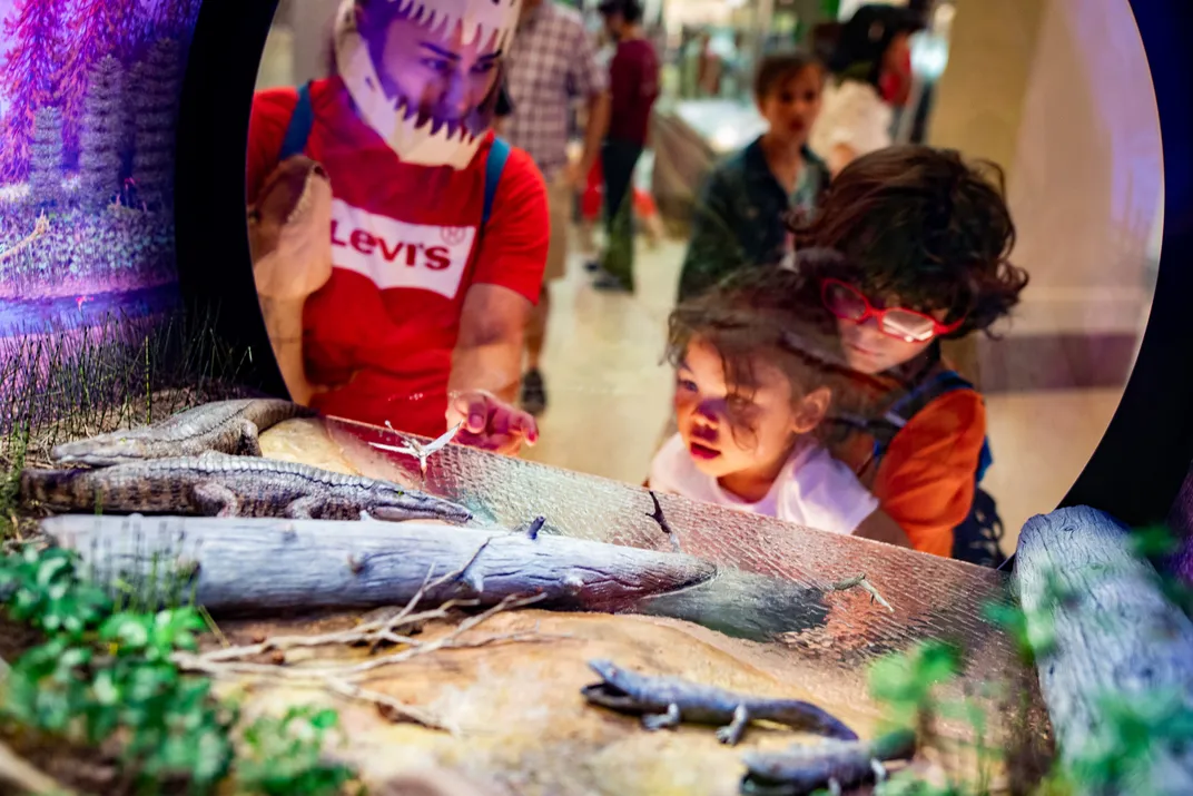 Three children look at a colorful recreation of an extinct ecosystem from 219-209 million years ago. 