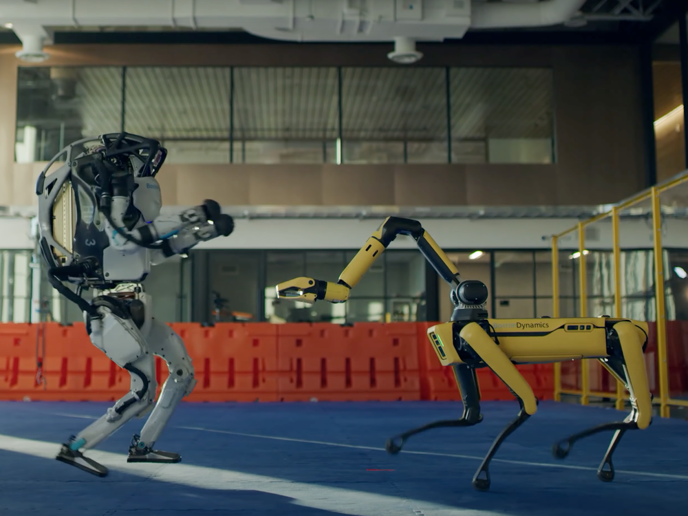 The humanoid Atlas robot dances on the left side of the image, and the canine-like Spot robot dances on the right 