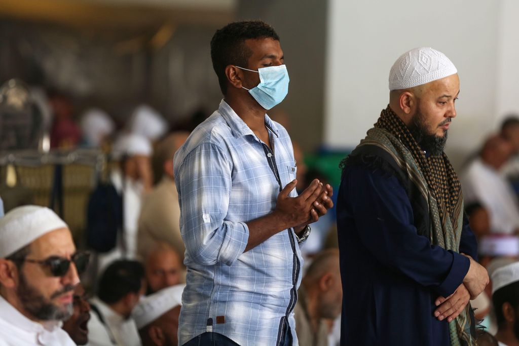 Muslim men pray at the Grand Mosque, one wearing a mask