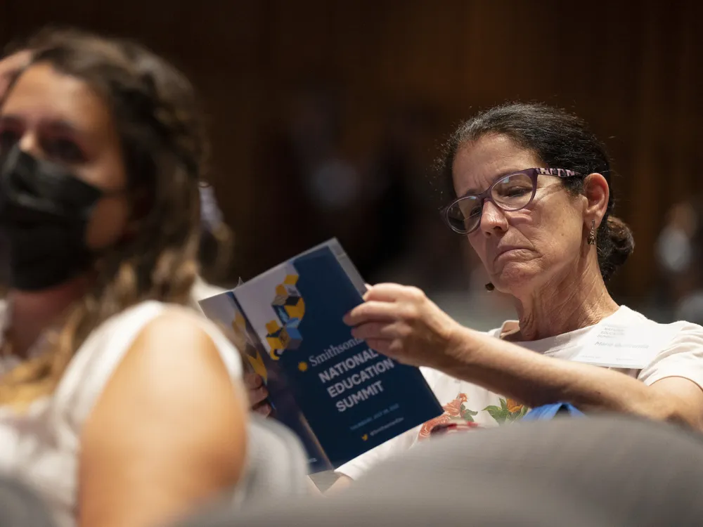 Woman with brown hair and glasses reads through a print program with the words "Smithsonian National Education Summit"