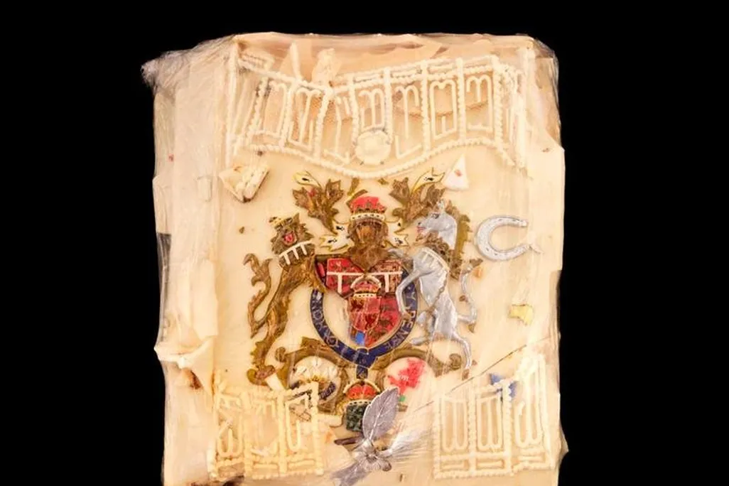 A closeup view of the cake slice, which is a square piece, yellowish, with cracked but intricate icing on top and a knight, gold leaf, and a laced icing border