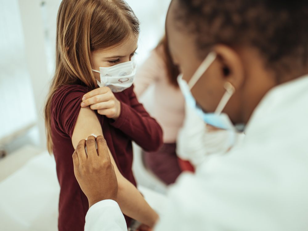 A female doctor wearing a mask vaccines a young girl wearing a mask