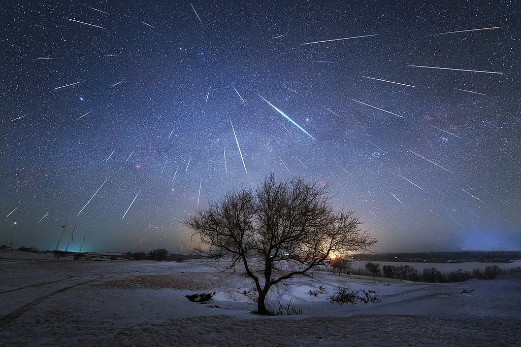 many meteors in the sky above a landscape with a bare tree