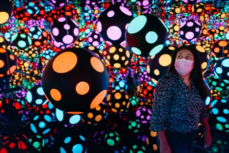 A museum patron enjoys Yayoi Kusama&#39;s latest work,&nbsp;Infinity Mirrored Room&mdash;My Heart Is Dancing into the Universe&nbsp;(2018), where paper lanterns and dots endlessly multiply inside the chamber.