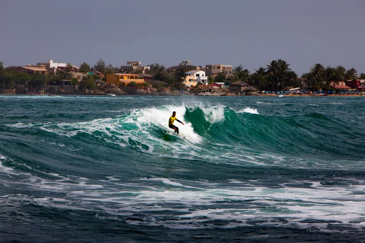 a surfer on a wave with some colorful buildings on the shoreline in the background