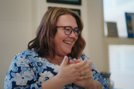 Teacher with short brown hair and glasses, wearing a blue shirt is smiling and clapping