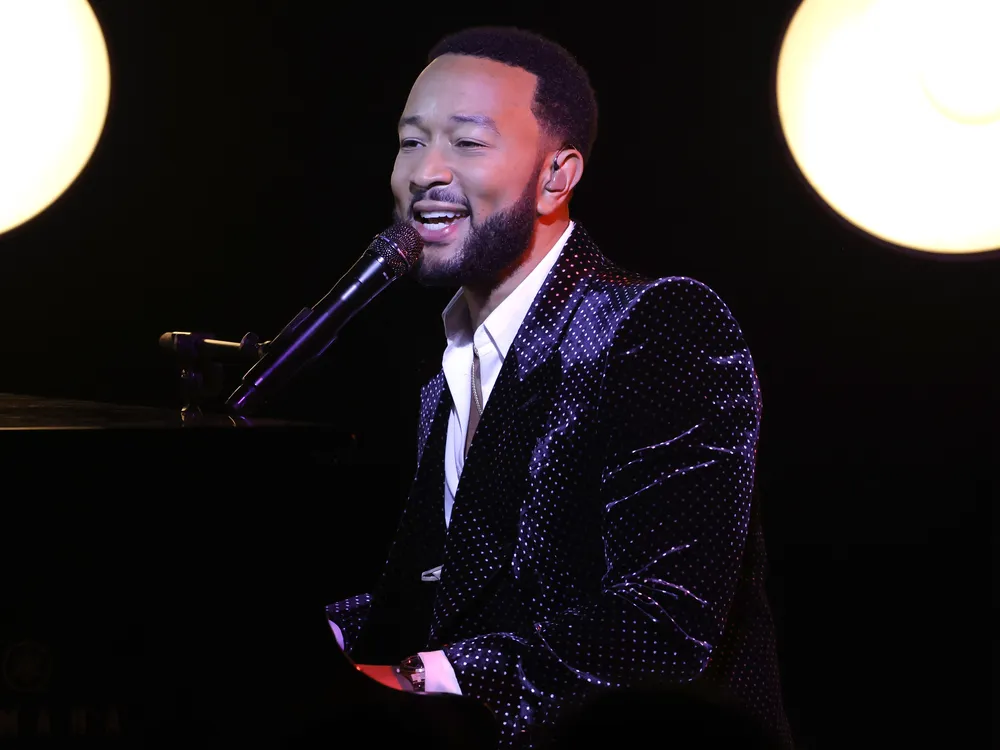 John Legend sitting at a piano singing in a microphone