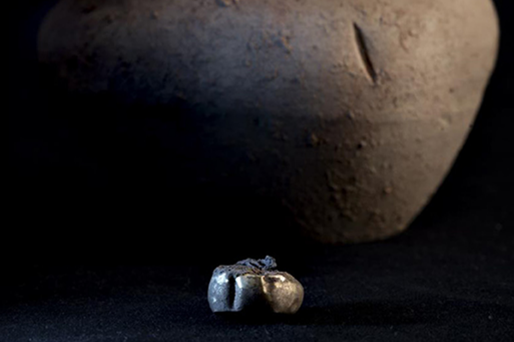 A golden earring sits in front of the brown pot it was discovered within.