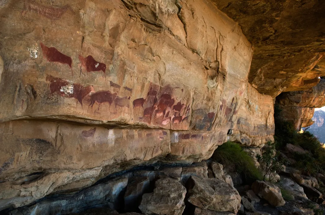 A rock cave wall with paintings of wildlife in dark red pigment