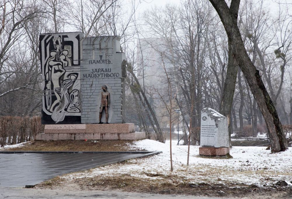 snowy view of a monument with a bronze statue of a man standing in front of a wall with Ukrainian writing