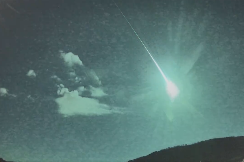 a bright green streak in the sky next to some clouds makes the entire night sky appear green