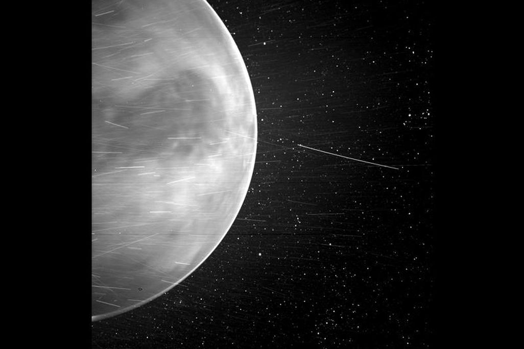 A letterboxed image with NASA's new Venus placed vertically at the center. Half of the planet is positioned on the left part of the picture with celestial objects zooming by and stars in the background