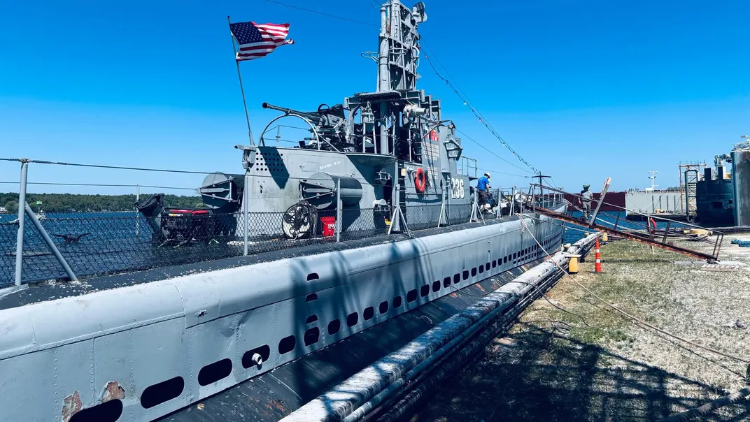A submarine floating atop water next to a dock with a ramp