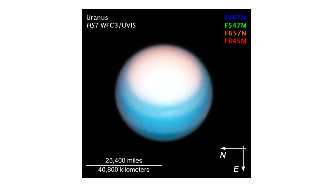 An image of uranus bathed in ultraviolet light. The planet looks blue with a large white spot towards its northern hemisphere