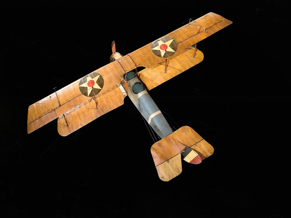 A wood and fabric World War I-era Curtis JN-4D aircraft is on display at the National Air and Space Museum. It has tan wings, and a brown and blue fuselage.