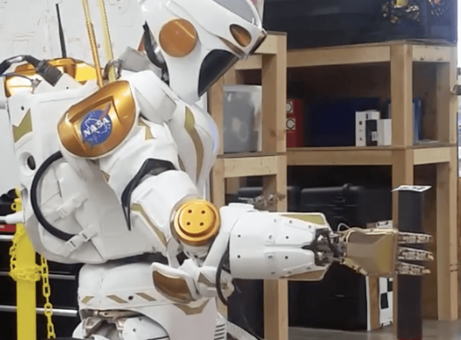A NASA Valkyrie robot picks up an item with its hand.
