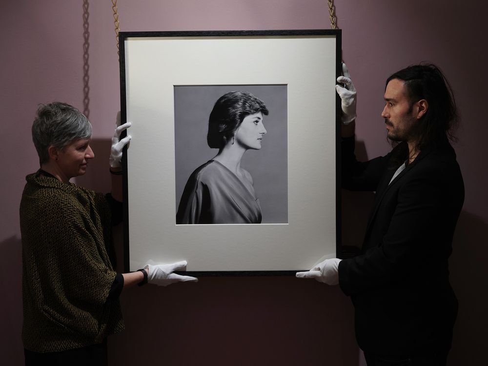 Two curators hanging up black and white portrait featuring profile of Princess Diana