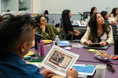 A man in a blue shirt looks at a photograph of archival images while several other people look toward a presentation