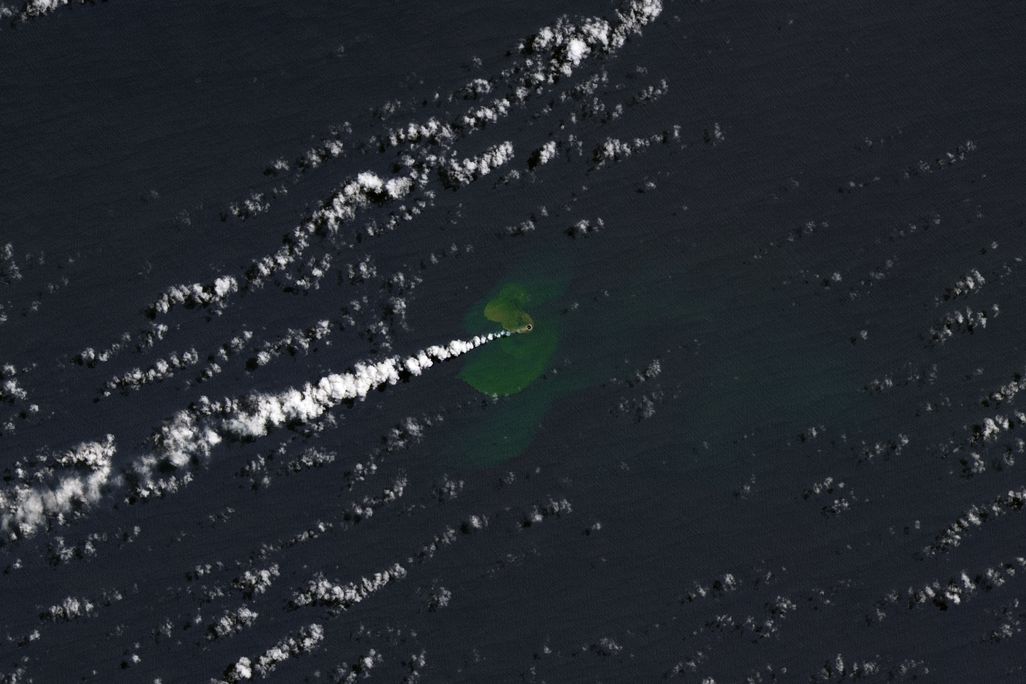 An aerial view of the Pacific Ocean shows a plume of ash from the recent eruption.