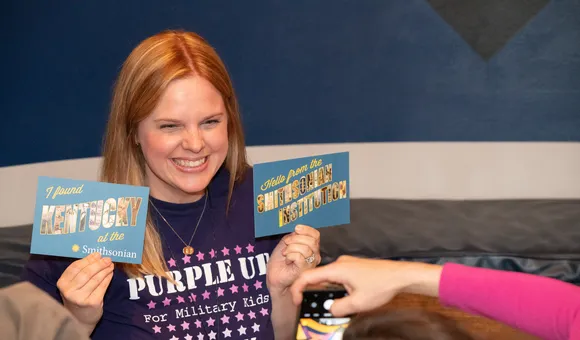 Woman smiling holds up two postcards
