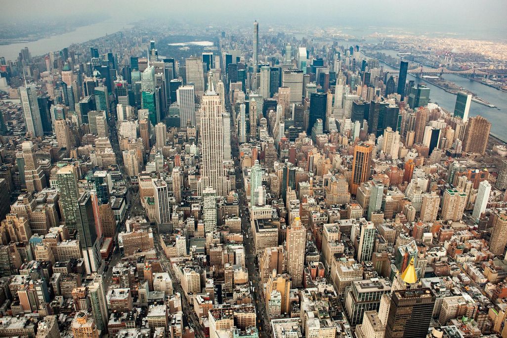An aerial photograph of New York City. There are endless rows of skyscrapers and shiny buildings, stretching back to the horizon.