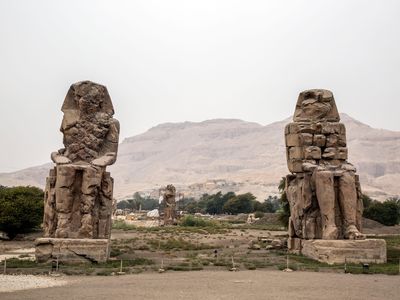 Statue of Memnon in the westbank in Luxor, with the community of Qurna in the background.