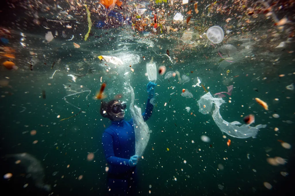 submerged diver with large and small plastic fragments in the water