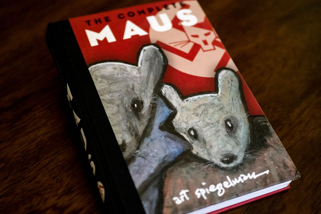 A hardcover edition of Maus, with two gray mice on its cover in front of a red background and swastika symbol
