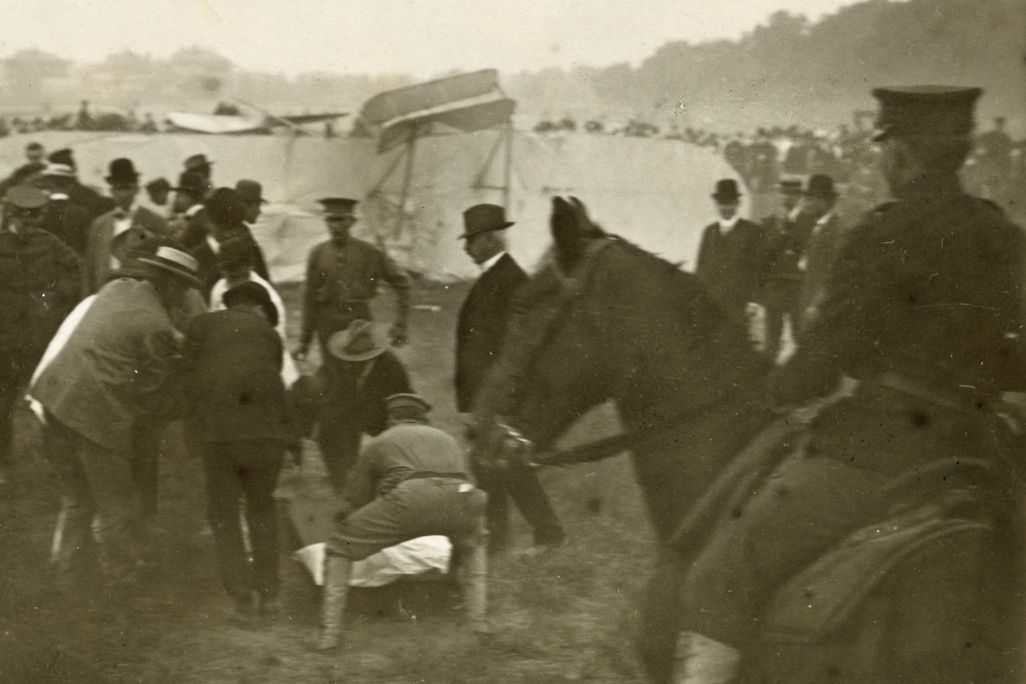 Bystanders crouch over Thomas Selfridge, pulled from the wrecked Wright Model A.