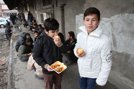 On 19 March 2017 in Serbia, 9-year-old Ibrahim and 11-year-old Abuzar, both from Afghanistan, eat food they received during a lunchtime meal distribution, outside dilapidated warehouse buildings at an informal squatter settlement known as The Barracks, in Belgrade, the capital.