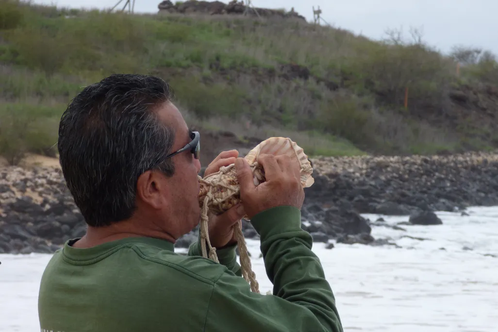 man blowing a conch shell