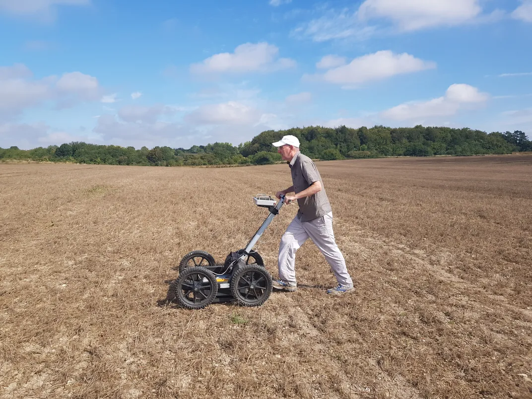 A man pushing a wheeled cart across a flat landscape