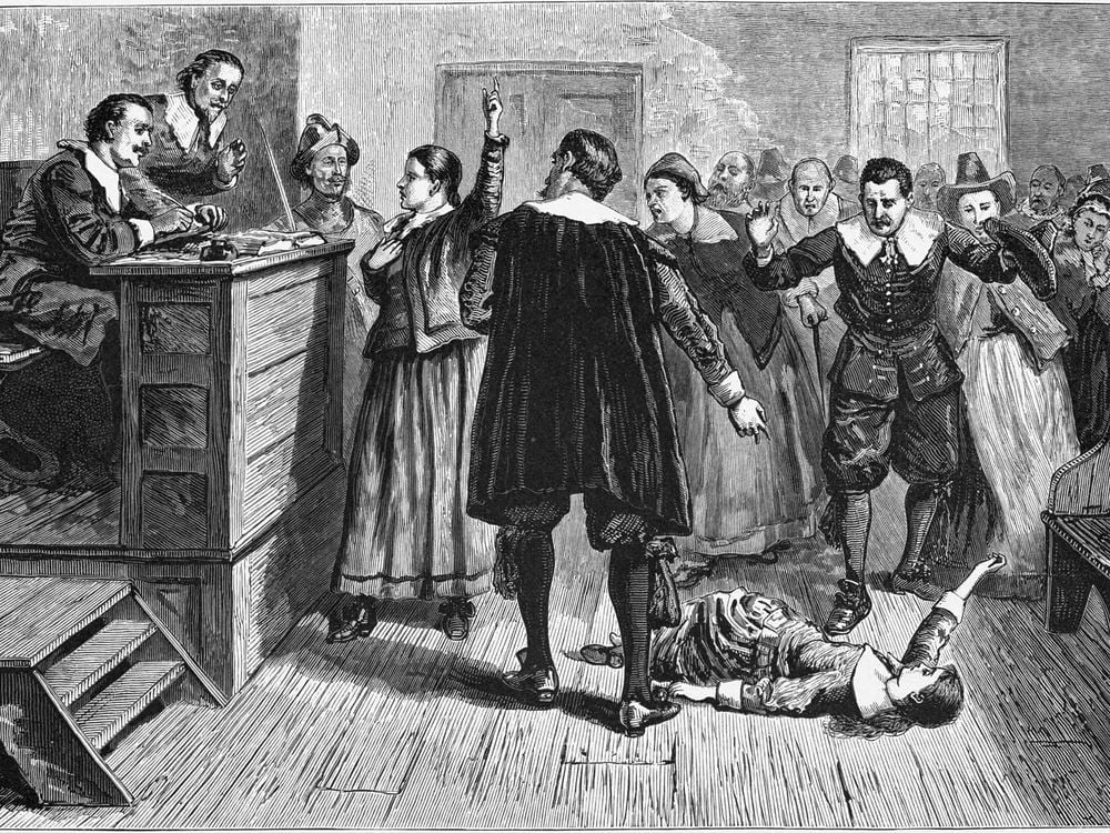 A black and white engraving of a courtroom scene; one woman stands in the center and raises a hand as though defending herself, while a young girl falls on the floor beneath a crowd of people