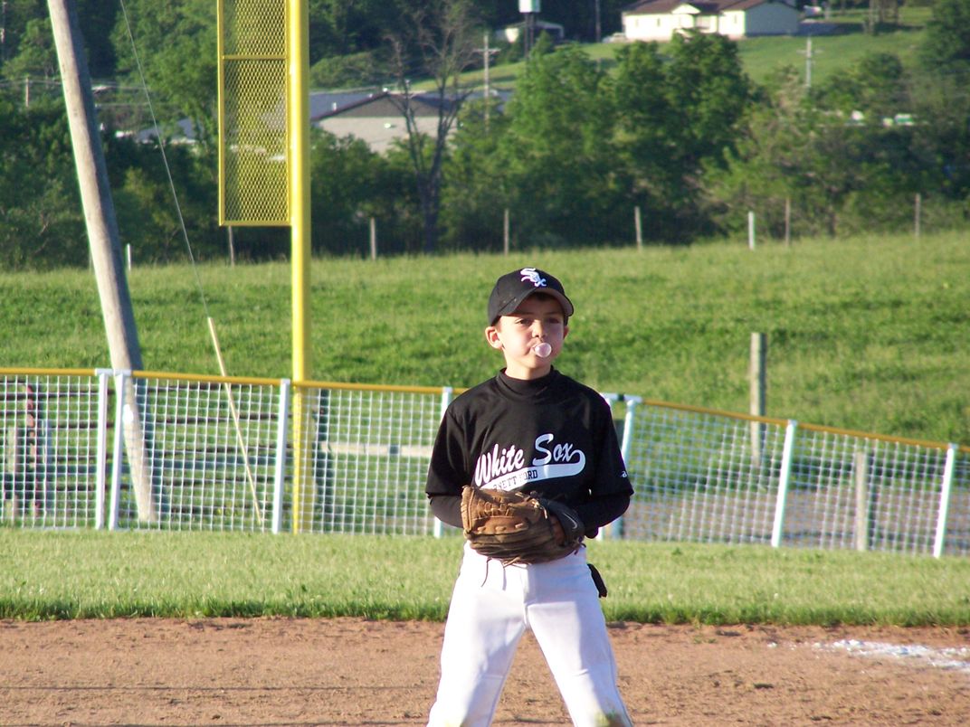 a young baseball player blows a bubble with chewing gum